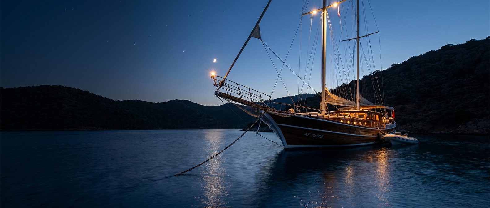 A boat anchored in a cove at dusk with its lights on