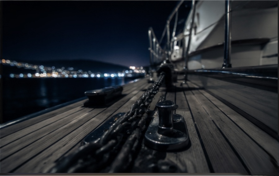 The deck of a boat lying at anchor at night, the anchor chain taut